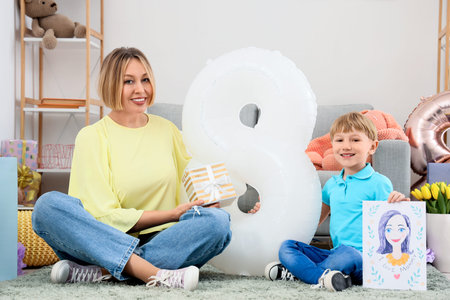 Little boy and his mother with gifts sitting at home. International Women's Day