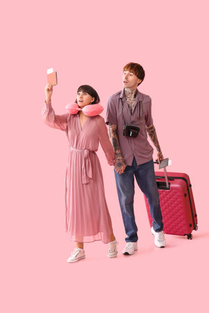 Couple of young tourists with passport and suitcase walking on pink backgroundの写真素材