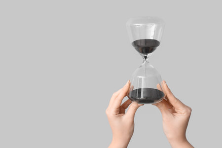 Female hands holding hourglass on gray backgroundの写真素材