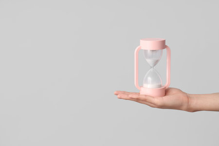 Female hand holding hourglass on gray background