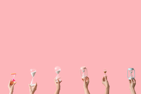 Female hands holding hourglasses on pink backgroundの写真素材