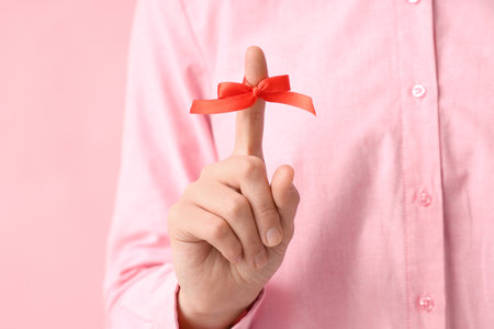 Woman with red bow on index finger against pink background. Reminder conceptの写真素材