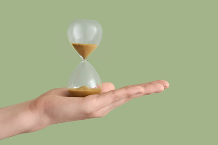 Female hand holding hourglass on green backgroundの写真素材