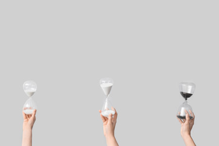 Female hands holding hourglasses on gray background