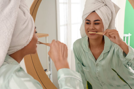 Young African-American woman after shower brushing teeth near mirror in bathroomの写真素材