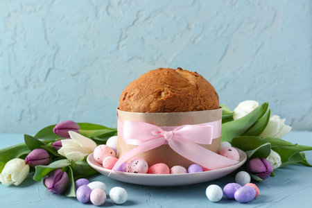 Plate with delicious Easter cake, painted eggs and tulip flowers on blue background