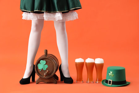 Woman in waitress costume with leprechaun's hat, barrel and glasses of beer on orange background. St. Patrick's Day celebrationの写真素材
