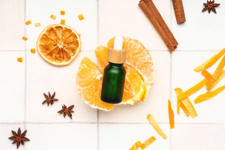 Composition with bottle of essential oil, orange and spices on light tile background