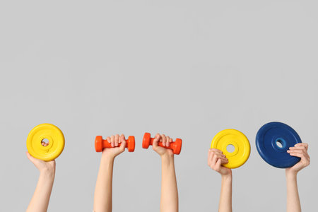Female hands with dumbbells and barbell plates on gray backgroundの写真素材