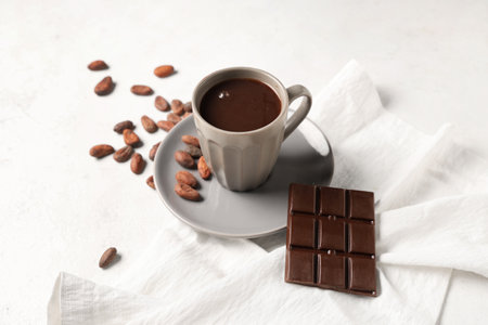 Plate with cup of tasty hot chocolate, cocoa beans and napkin on white backgroundの写真素材