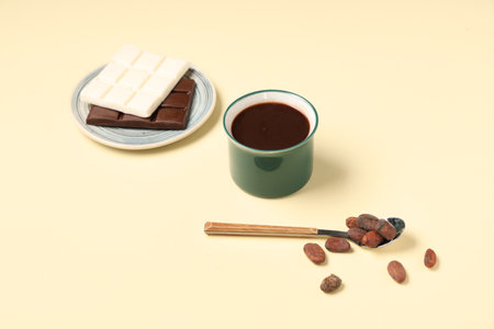 Cup of tasty hot chocolate and spoon with cocoa beans on light yellow backgroundの写真素材