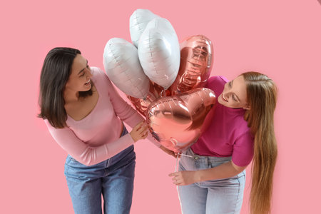 Young lesbian couple with balloons on pink background. Valentine's Day celebrationの写真素材