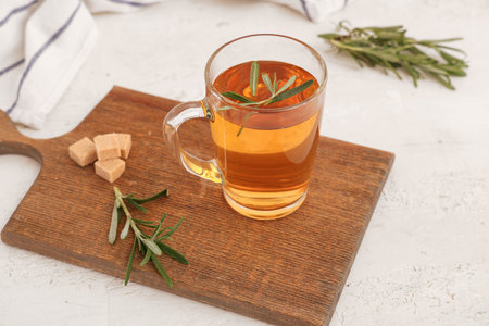 Wooden board with glass cup of hot rosemary tea and sugar on white backgroundの写真素材
