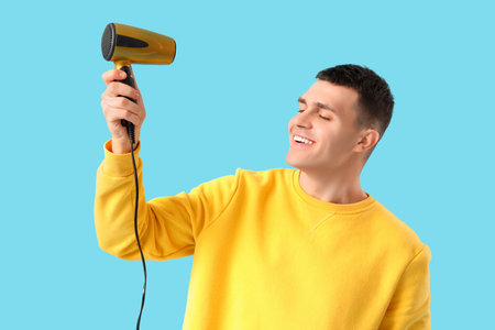 Handsome young man with hair dryer on blue backgroundの写真素材