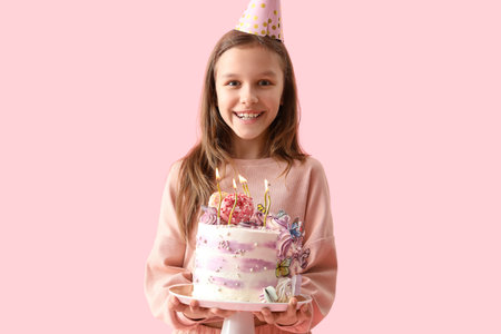 Cute little girl in party hat with Birthday cake on pink backgroundの写真素材