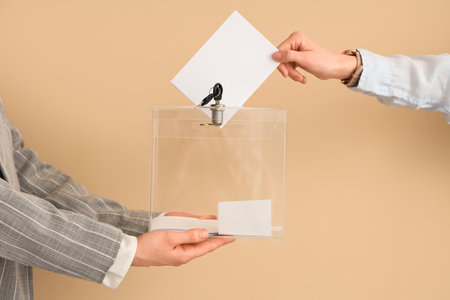 Hand putting voting paper into ballot box on beige background. Election conceptの写真素材