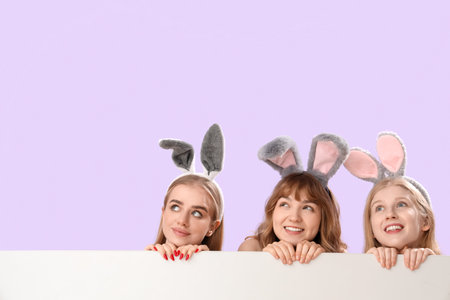 Young girls with Easter bunny ears and blank poster on lilac backgroundの写真素材