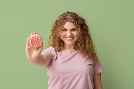 Beautiful young woman with hair scalp massager on green backgroundの写真素材