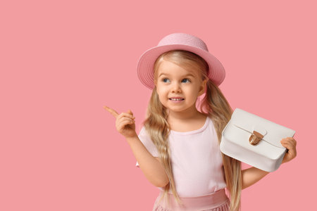 Cute little girl with stylish white bag pointing at something on pink backgroundの写真素材