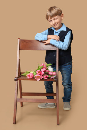 Cute little boy and bouquet of beautiful tulips on chair against brown background. International Women's Dayの写真素材