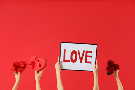 Female hands holding frame with the word LOVE, heart-shaped gift boxes and roses on red background. Valentine's Day celebrationの写真素材