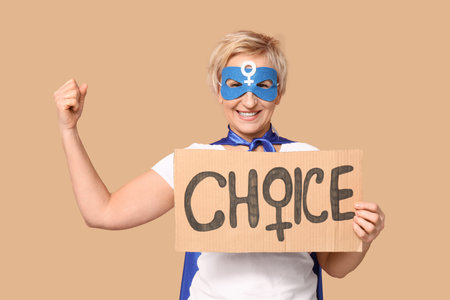 Mature woman in superhero costume holding cardboard with word CHOICE on beige backgroundの写真素材