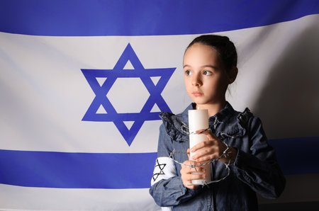 Little Jewish girl with burning candle and barbed wire against flag of Israel. International Holocaust Remembrance Dayの写真素材