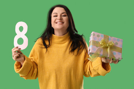 Beautiful happy mature woman with gift box and paper number 8 on green background. International...