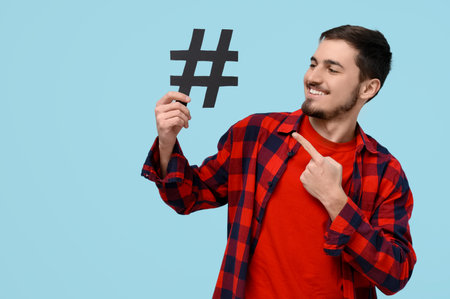 Handsome young man pointing at hashtag sign on blue backgroundの写真素材