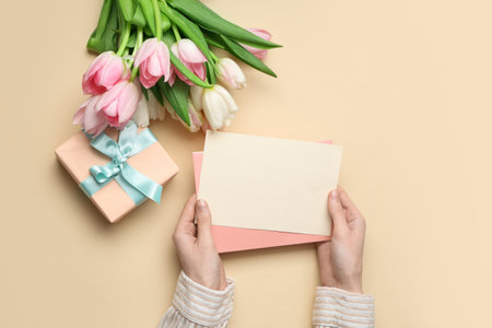 Female hands with blank card, gift box and bouquet of beautiful tulips on yellow background. International Women's Dayの写真素材