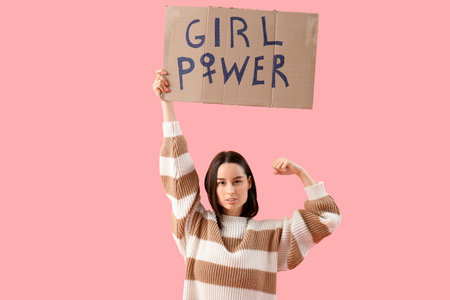 Beautiful young woman holding paper with text GIRL POWER and showing muscles on pink background. Women history monthの写真素材