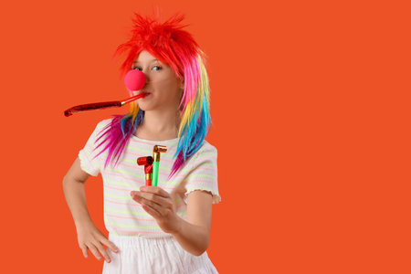 Funny girl in clown costume with party whistle on orange background. April Fool's Day celebrationの写真素材