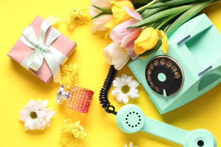 Retro telephone with gift box, perfume and beautiful flowers on yellow background. International Women's Dayの写真素材