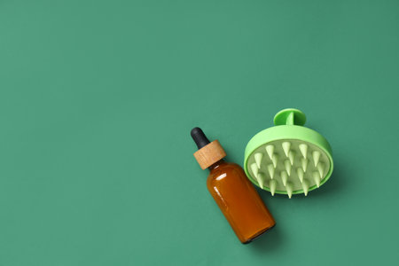 Hair scalp massager and bottle of cosmetic oil on green backgroundの写真素材