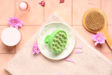 Hair scalp massager with different cosmetic products, body brush and chrysanthemum flowers on pink tile backgroundの写真素材