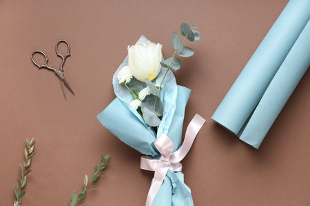 Mini bouquet of beautiful spring flowers in wrapping paper with eucalyptus and scissors on brown background. International Women's Dayの写真素材