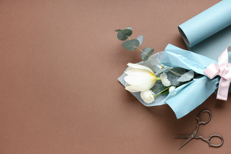 Mini bouquet of beautiful spring flowers in wrapping paper with scissors on brown background. International Women's Dayの写真素材