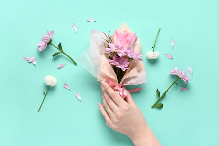 Female hand with mini bouquet of beautiful spring flowers in wrapping paper on turquoise background. International Women's Dayの写真素材