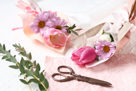 Mini bouquets of beautiful spring flowers in wrapping paper with eucalyptus and scissors on white background. International Women's Dayの写真素材