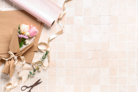 Composition with mini bouquet of beautiful spring flowers in wrapping paper, ribbon and scissors on beige tile background. International Women's Dayの写真素材
