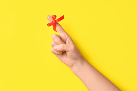 Female hand with red bow on index finger against yellow background. Reminder conceptの写真素材