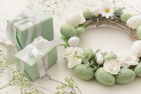 Composition with Easter wreath made of green painted eggs and bunny figurine and gifts on white...