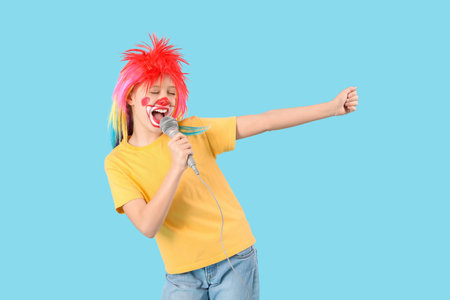 Funny girl in clown costume with microphone on blue background. April Fool's Day celebrationの写真素材