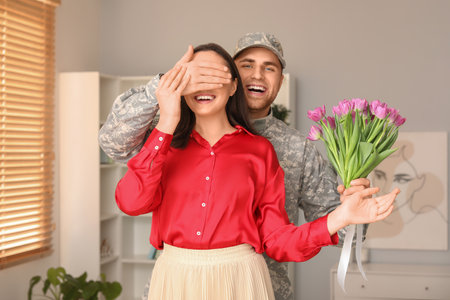 Man in military uniform covering eyes of his wife at home. Valentine's Day celebrationの写真素材