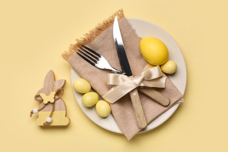 Stylish table setting with Easter eggs, napkin and cutlery on yellow backgroundの写真素材