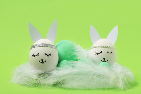 Pack of painted Easter eggs with paper bunny ears and feathers on green background