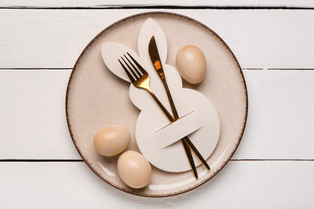 Beautiful table setting with Easter eggs, paper bunny and cutlery on white wooden background
