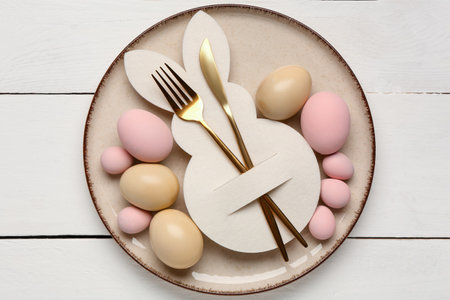 Beautiful table setting with Easter eggs, paper bunny and cutlery on white wooden backgroundの写真素材