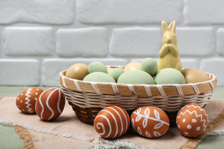 Wicker basket with painted Easter eggs and bunny on gray table near white brick wall