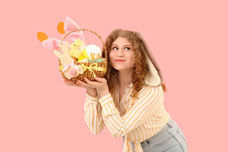 Beautiful young happy woman in bunny ears with Easter basket on pink background